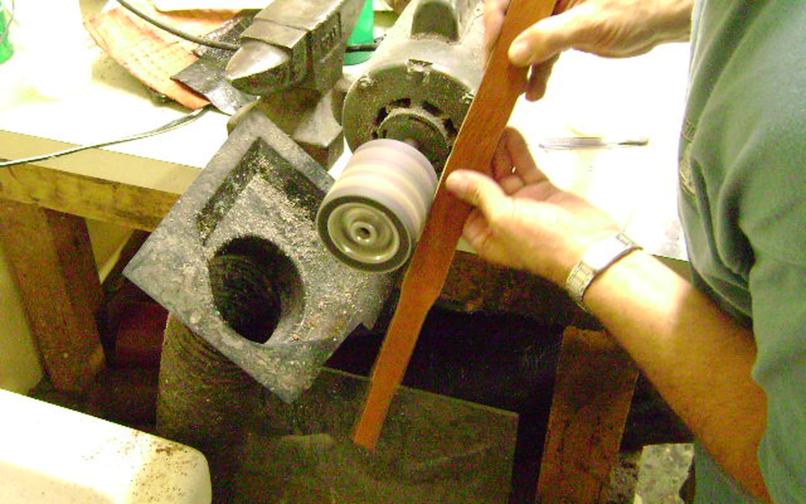 Finishing the edge of a leather belt strap on the polishing wheel at the workbench.